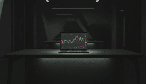 Trader reviewing candlestick charts on a laptop at a dark desk